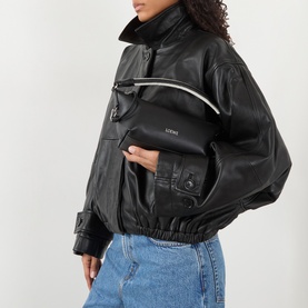Model carrying Loewe Cala Top Handle Pouch Bag in black, silver-tone hardware, worn crossbody over black leather jacket with blue jeans.