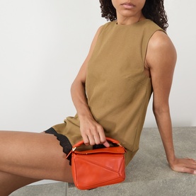 Model carrying Loewe Featherlight Puzzle Mini Crossbody Bag in Deep Saffron, gold-tone hardware, geometric silhouette, styled with a tan sleeveless