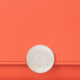 Loewe wallet in Sunrise Orange calfskin, close-up of embossed Anagram logo on circular white clasp detail