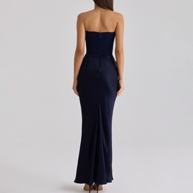 Model wearing House of CB navy strapless maxi dress with fitted bodice, ruched waist detail and fishtail hem, back view