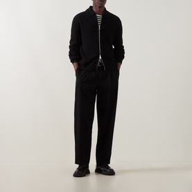 Model wearing Seven Jeans Black Polo Collar Zip Sweater with black trousers and striped top underneath, styled with black loafers.
