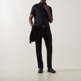 Model wearing Boggi Milano Supima Solid Polo Shirt in black with matching trousers, black belt, and leather shoes, jacket draped over hand.