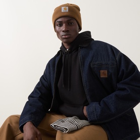 Model with Carhartt Watch Logo Beanie Hat in brown, featuring turned-up brim and logo badge. Styled with navy jacket and black hoodie.