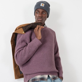 Model with Carhartt Watch Logo Beanie Hat in Styx grey, styled with a mauve ribbed knit jumper and tan jacket over the shoulder.