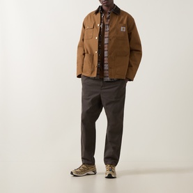 Model wearing Carhartt Hamilton Brown casual jacket, styled with checked shirt, dark trousers and trail trainers.