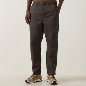 Model wearing Carhartt Casual Trouser in Shungite brown, relaxed fit with elasticated waist, styled with beige trail trainers.