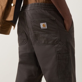 Model wearing Carhartt Casual Trousers in Shungite, close-up of cargo pocket detail with logo patch and elasticated waistband.
