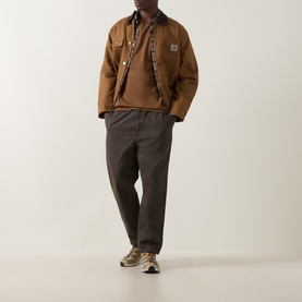 Model wearing Carhartt Casual Trouser in Shungite, styled with a brown workwear jacket and trail trainers.