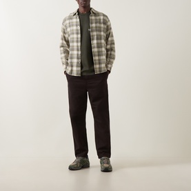 Model wearing Carhartt Casual Trousers in Tobacco, styled with a plaid overshirt, green tee and grey trainers.