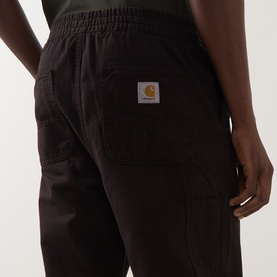 Model wearing Carhartt Casual Trousers in Tobacco, showing rear patch pocket detail with logo badge and elasticated waistband.
