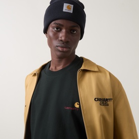 Model wearing Carhartt Crew Neck T in Raven, styled with a mustard coach jacket and black beanie hat.