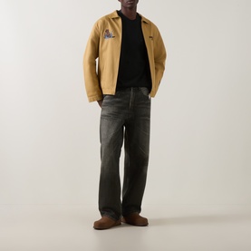 Model wearing Carhartt Crew Neck T in Raven black, styled with a tan workwear jacket and dark grey relaxed-fit jeans.