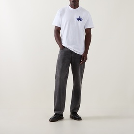 Model wearing Carhartt New Tools Logo Back Graphic T-Shirt in white with grey jeans and black leather shoes.