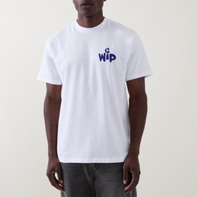 Model wearing Carhartt New Tools Logo Back Graphic T-Shirt in white, with navy WIP chest logo, crew neck, short sleeves, paired with grey jeans.
