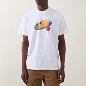 Model wearing Carhartt white crew neck T-shirt with food graphic print, styled with tan trousers.