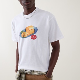 Model wearing Carhartt white crew neck T-shirt with cheese plate graphic print, styled with plaid shirt underneath and silver chain necklace.