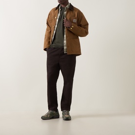 Model wearing Carhartt Crew Neck T in Cypress green, styled with tan chore coat, plaid shirt, dark trousers and grey trainers.