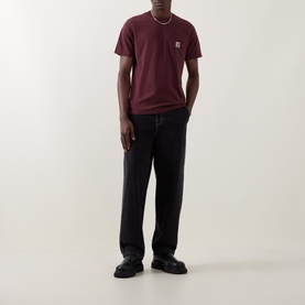 Model wearing Carhartt Logo Chest Pocket T-Shirt in Amarone, styled with black trousers and black shoes.