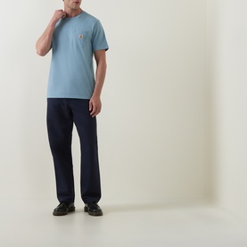Model wearing Carhartt Crew Neck T in Citadel blue with chest pocket logo, styled with navy trousers and dark shoes.