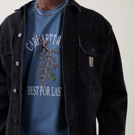 Model wearing Carhartt Crew Neck T in Icesheet blue with tree graphic print, styled with a black denim overshirt.