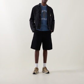 Model wearing Carhartt Crew Neck T in Icesheet blue with graphic print, styled with black denim jacket, black shorts and tan trainers.
