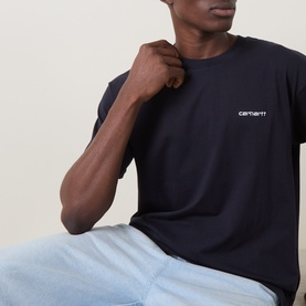 Model wearing Carhartt crew neck T-shirt in dark navy with white chest logo, styled with light blue trousers.