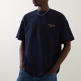 Model wearing Carhartt Signature Script Logo T-Shirt in dark navy, with gold embroidered script logo on chest, round neck, short sleeves.