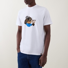 Model wearing Carhartt white crew neck T-shirt with bear graphic holding a horseshoe, styled with blue jeans.