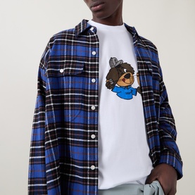 Model wearing Carhartt white crew neck T-shirt with bear graphic print, styled with blue plaid overshirt