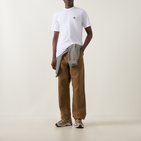 Model wearing Carhartt white crew neck T-shirt with small red heart logo, styled with tan trousers and grey jacket