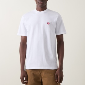 Model wearing Carhartt white crew neck T-shirt with small red heart logo embroidery on chest, styled with tan trousers