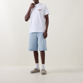 Model wearing Carhartt white crew neck T-shirt with small chest graphic, styled with light blue denim shorts and grey slip-on shoes.
