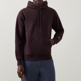 Model wearing Carhartt hoodie in Palisander, gold logo detail on sleeve, paired with navy trousers