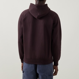 Model wearing Carhartt hoodie in Palisander, rear view, with blue cargo trousers. Relaxed fit with drawstring hood and raglan sleeves.
