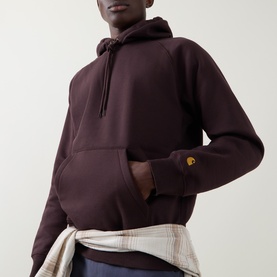 Model wearing Carhartt hoodie in Palisander with gold logo detail, styled with a plaid shirt tied at the waist