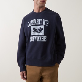 Model wearing Carhartt dark navy cotton sweatshirt with large graphic logo print, styled with tan trousers