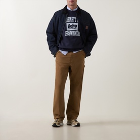 Model wearing Carhartt Dark Navy cotton sweatshirt with graphic print, styled with tan carpenter trousers and a white shirt underneath.