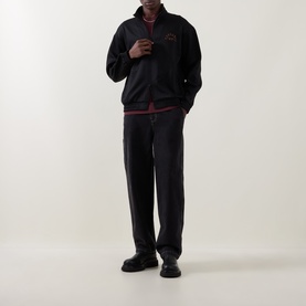 Model wearing Carhartt black zip-through sweat with red graphic chest logo, styled with matching black trousers and black leather shoes.