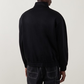 Model wearing Carhartt black zip-through sweatshirt, back view, styled with dark contrast-stitch jeans.