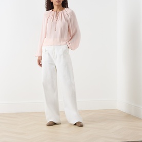 Model wearing FRAME DENIM Taffy silk blouse with voluminous sleeves and tie neck, styled with wide-leg white trousers
