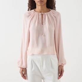 Model wearing Frame Denim Taffy silk blouse with gathered neckline, tassel tie, and billowy long sleeves, styled with white trousers