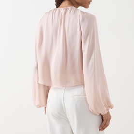 Model wearing FRAME DENIM Taffy silk blouse, back view, with balloon sleeves and gathered neckline, styled with white trousers.