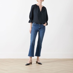 Model wearing FRAME DENIM navy cotton blouse with puff sleeves and V-neck, styled with cropped flare jeans and black mules.