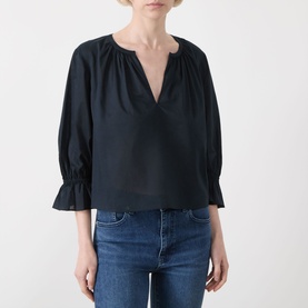 Model wearing Frame Denim navy cotton blouse with V-neckline, gathered detailing and fluted sleeves, styled with blue denim jeans.