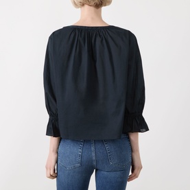 Model wearing Frame Denim navy cotton blouse, back view, featuring gathered neckline and fluted sleeves, styled with blue jeans