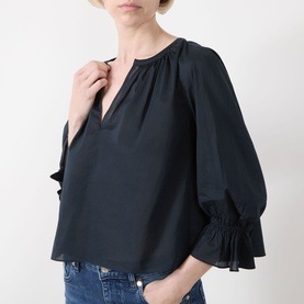 Model wearing Frame Denim navy cotton blouse with V-neckline, gathered detail and elasticated cuffs, styled with blue jeans.