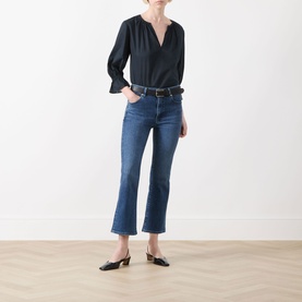 Model wearing FRAME DENIM navy cotton blouse with V-neck and fluted sleeves, styled with dark wash cropped flare jeans and black mules