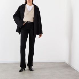 Model wearing FRAME DENIM Reboot Bootcut Jeans in black, high-rise fit, styled with a black oversized coat and beige knit vest.