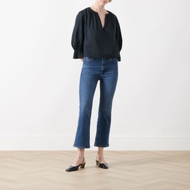 Model wearing FRAME DENIM Crop Boot jeans in Sonnet, a mid-blue wash with raw hem, styled with a black blouse and black mules.