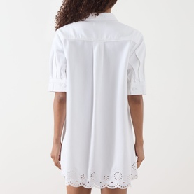 Model wearing FRAME DENIM white cotton-lyocell shirt dress, back view, with broderie anglaise hem detail and short sleeves.